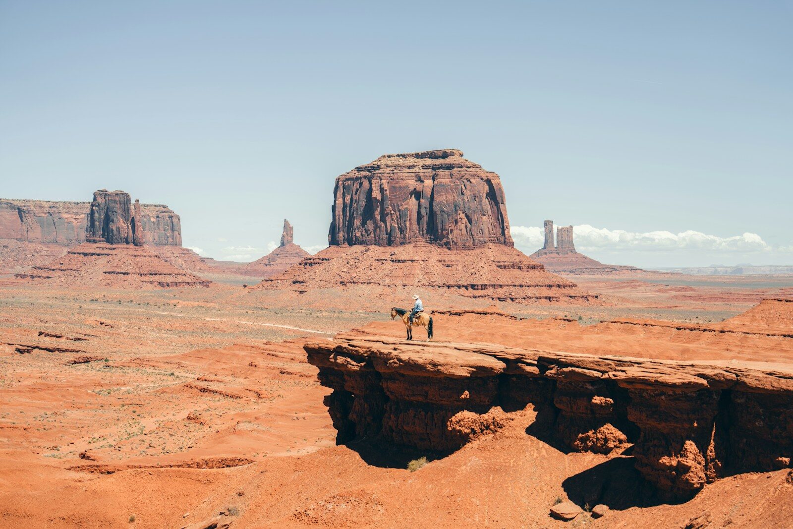 Lone figure stands on cliff edge in monument valley.